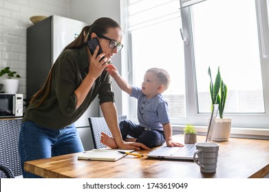 Freelancer Mother Trying To Work From Home While Babysitting With Kid. Mom Is Talking On The Phone While Her Child Is Take It Out Of Hand.