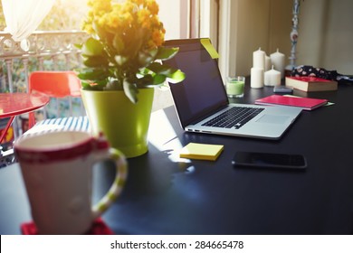 Freelancer Needs Workstation, Workplace With Open Laptop Computer, Smart Phone, Notebook, Cup And Pot Of Flowers, On-line Learning Or Distance Work Concept, Modern Table At Window In Home Interior