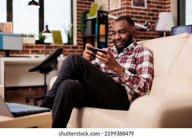 Freelancer Playing Online Gaming Competition On Smartphone, Having Fun With Video Games And Sitting On Couch. Enjoying Remote Internet Game Play On Mobile Phone App, Working On Freelance Job.