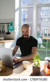 Freelancer programmer working from home on kitchen and using laptop. Bearded man working with a computer, prints text on keyboard. Self entrepreneur sitting and working at his modern apartment. - Shutterstock ID 1780976180