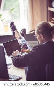 Freelancer Putting Legs In Pajamas And Slippers On Table. Home Office, Man Typing On Laptop. Toned Image.