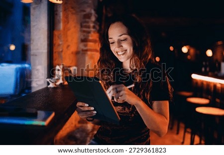 Freelancer smiling while writing on tablet, showcasing productivity, joy and emotional satisfaction from working with digital tools in relaxed modern setting.