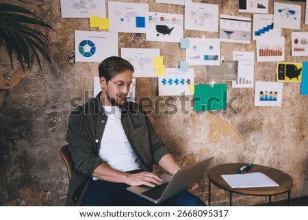 Freelancer using laptop in front of idea wall, immersed in refining UX concept and pushing forward agile strategy for digital product in modern tech-driven environment.