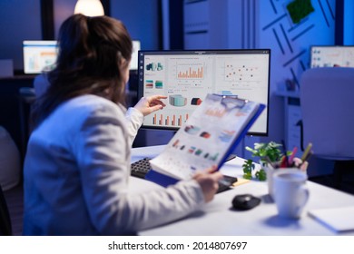 Freelancer woman comparing graphics from clipboard with grafics from computer at business office. Tired focused employee using modern technology network wireless working on project solution