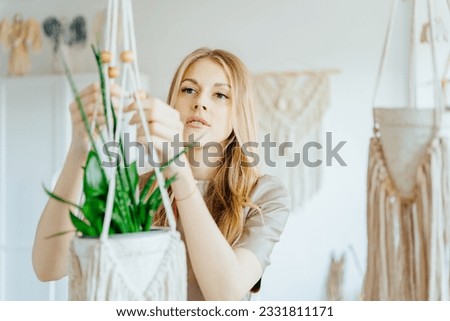 Freelancer woman working on half-finished macrame piece, Blond craft woman holding a potted plant in macrame suspending basket holder. Creative knitting concept.