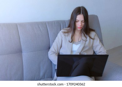 Freelancer woman working typing on laptop at home sitting on couch, freelance distant work on quarantine. Coronavirus pandemic. Self empoyed businessman, COVID-19 epidemic. Wearing suit Casual Style.