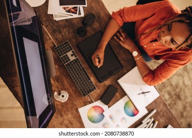 Freelancer working at her creative workstation. High angle view of a female graphic designer drawing on a digital tablet. Creative young woman working on a new design in her home office.