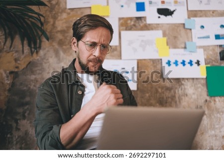 Freelancer working remotely with serious expression, reviewing UX model on laptop and adjusting product features to align with data-driven design strategy in agile setup.