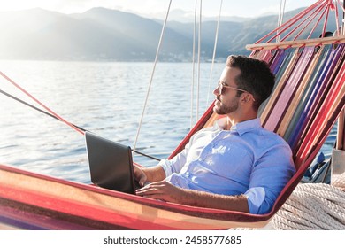 Freelancer working in traveling, using laptop, Internet. Man with computer in beach hammock. Sea summer vacation on yacht. Workplace on nature outdoors. Business trip, successful lifestyle - Powered by Shutterstock