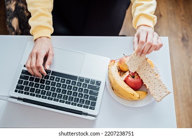 Freelancer Young Woman Eating Healthy Food When Working From Home. Woman Eating Healthy Grain Snacks And Fruits While Working With Laptop At Home Office