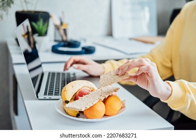 Freelancer Young Woman Eating Healthy Food When Working From Home. Woman Eating Healthy Grain Snacks And Fruits While Working With Laptop At Home Office