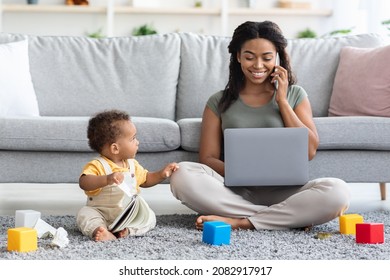 Freelancing With Baby. Smiling Black Woman Working On Laptop And Taking Care Of Her Infant Child At Home, African American Mother Using Computer And Talking On Cellphone With Client, Copy Space