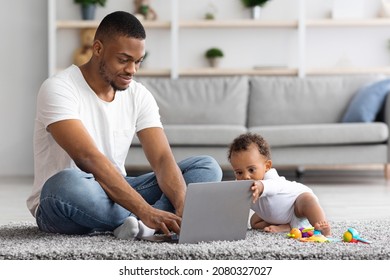 Freelancing With Baby. Young African American Man Working On Laptop And Taking Care Of His Infant Child At Home, Black Father Using Computer For Online Work And Babysitting Toddler Kid, Copy Space