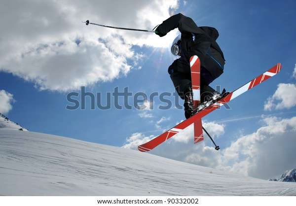 A free-ride ski jumper, with skis crossed against\
a blue sky with clouds
