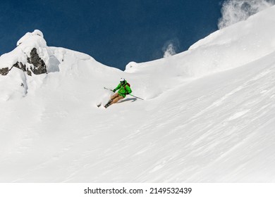 freeride skier in bright green ski suit energetically rides down on snow-covered mountain slope. Freeride skiing concept.