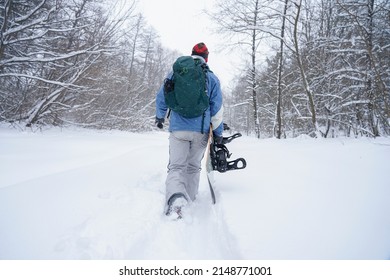 The freerider guy walks through the snow powder. He is holding a snowboard