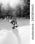 Freerider with snowboard in hands at snowy spruce forest at sun winter day. Christmas Holidays in Carpathian Mountains, Ukraine. Remote location. Black and white toned image.