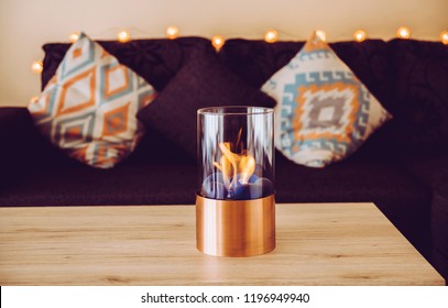 Freestanding Portable Glass And Copper Metal Fireplace Burning Bio Ethanol Gas On Living Room Wooden Table. Autumn Comfortable Colorful Cozy Home Set.
