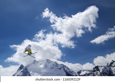 Freestyle ski jumper with crossed skis against snowy mountains 