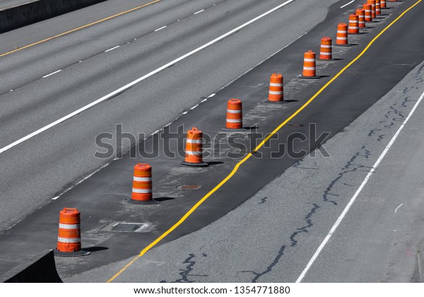 Freeway construction zone with a concrete\
roadway repaved with black asphalt, and line of orange barrel\
cones, in a transportation\
background