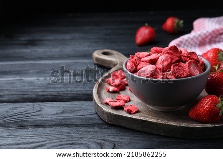 Freeze dried and fresh strawberries on black wooden table. Space for text