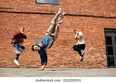 Freeze Frame Of All Male Breakdancing Team Jumping In Air And Posing Against Brick Wall