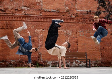 Freeze Frame Of All Male Breakdancing Team Jumping In Air Against Brick Wall Outdoors