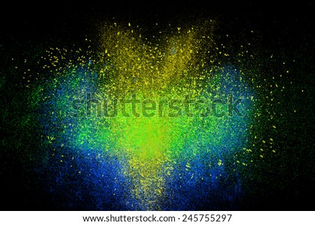 Freeze motion of colorful powder exploding, isolated on black, dark background. Abstract design of dust cloud. Particles explosion screen saver wallpaper with copy space. Vivid yellow blue green ash