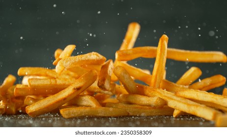 Freeze motion of flying french fries on dark background. Concept of junk unhealthy food, studio shot.