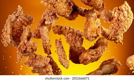 Congelar el movimiento de piezas voladoras de pollo frito sobre fondo dorado. Concepto de levitación de alimentos.