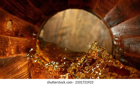 Freeze motion of splashing whisky in wooden barrel. Concept of pouring whisky, rum or cognac inside a keg. Alcoholic beverage background.