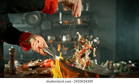 Freeze Motion of Wok Pan with Flying Ingredients in the Air. Chef Pouring Salt. Kitchen on Background. - Powered by Shutterstock