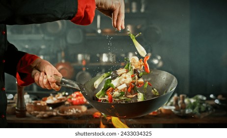 Freeze Motion of Wok Pan with Flying Ingredients in the Air. Chef Pouring Salt. Kitchen on Background. - Powered by Shutterstock