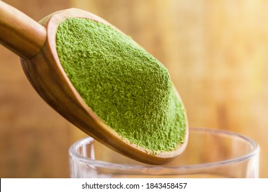 Freeze-dried Organic Wheat Grass Powder, Nutritional Supplement On A Wooden Tablespoon Over Glass Of Water.