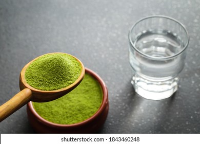 Freeze-dried Wheatgrass Powder, Nutritional Supplement On A Wooden Tablespoon And Glass Of Water.