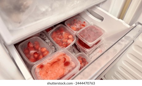 Freezer and frozen strawberries and raspberries in transparent plastic containers. Close-up