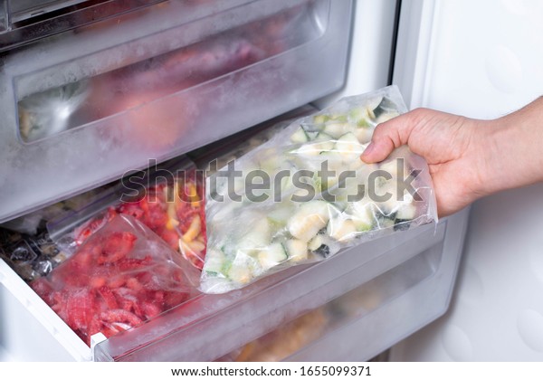 Freezer and frozen vegetables, a person taking\
food from the freezer,\
closeup