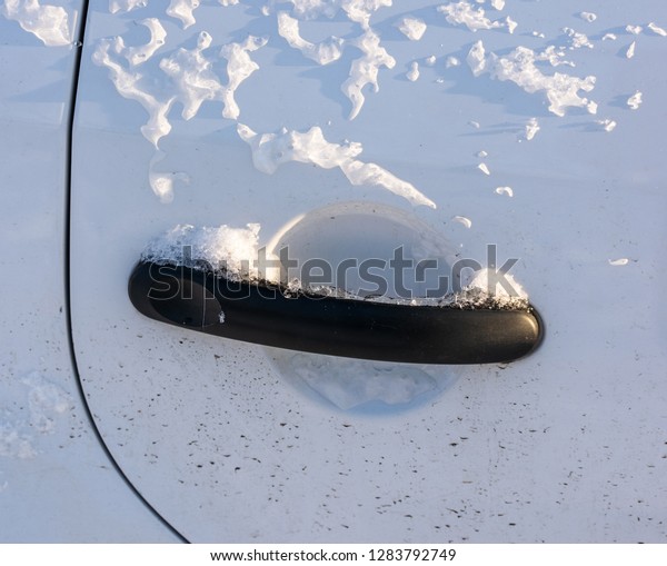 Freezing of the car door\
handle closeup. Black car door handle on white car door froze up\
after rain with wet snow. Can\'t open the door. Сar operation in\
winter concept.