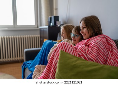 Freezing children wrapped in warm blankets while sitting on sofa in cold living room. Sisters Trying To Keep Warm Under Blanket At Home. Heating season. Recession, inflation energy crisis concept - Shutterstock ID 2221121021