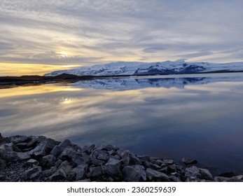 Freezing cold lake with snowy hills in distance, golden hour colored sky in iceland. with frozen water. Beautiful wilderness within northern region landscape and icelandic nature. - Shutterstock ID 2360259639