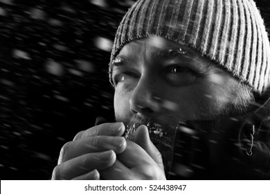 Freezing Cold Man Standing In A Snow Storm Blizzard Trying To Keep Warm. Wearing A Beanie Hat And Winter Coat With Frost And Ice On His Beard And Eyebrows. Black And White.