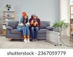 Freezing people in winter jackets sitting on sofa at home. Sad warmly closed husband abd wife feeling cold and trying to warm up. Heating problems, power crisis concept