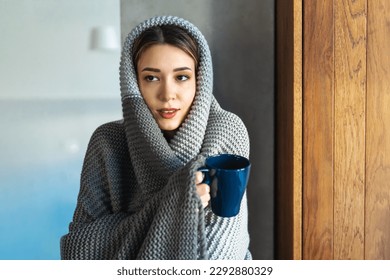 Freezing woman covered with a cozy blanket. Female wrapped in warm blanket, drinking hot drink.