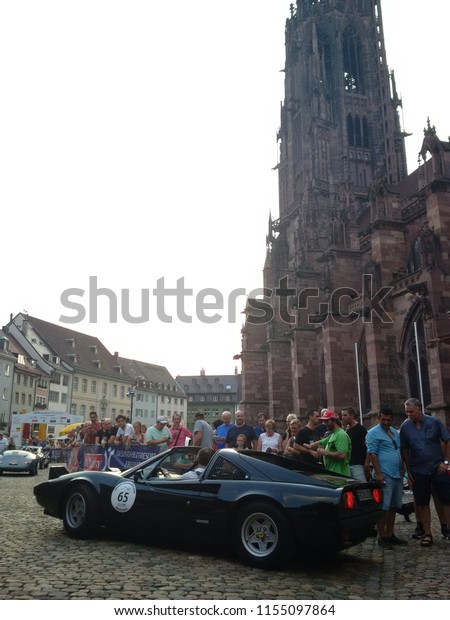 FREIBURG, GERMANY - AUGUST\
3, 2018: A 1978 Ferrari 308 GTS approaches the finish line at the\
Schauinsland Klassik 2018 classic car rally in front of the\
Freiburg Minster.