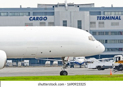 Freight Cargo Airplane In The Parking Lot Of The Airport, Against The Background Of The Cargo Terminal Of The Aerodrome Building