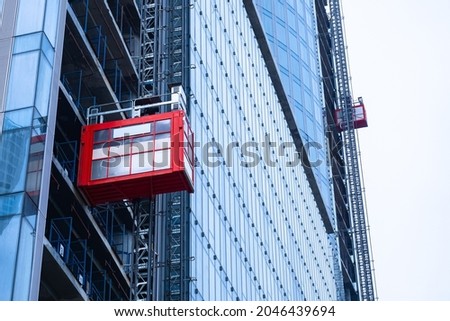 Freight construction elevator ascends to top of a skyscraper. Temporary elevator on a building under construction. Construction of skyscrapers. Red temporary elevator in a building under erection.