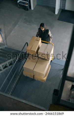 Freight handler transporting goods on wheeled cart in warehouse facility