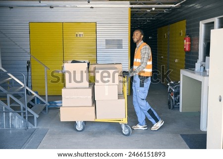 Freight handler transporting goods on wheeled cart in warehouse