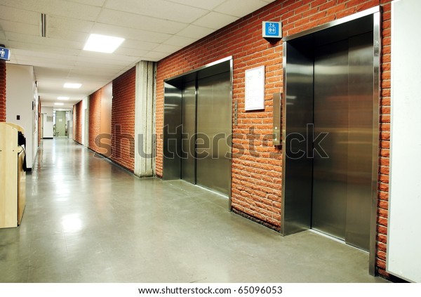Freight\
and regular steel door elevators with signs in an empty hallway of\
modern building. Can be office, school,\
hospital.
