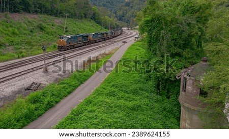 A freight train is captured in motion on a set of railway tracks that lead to an old, abandoned tower in the background
